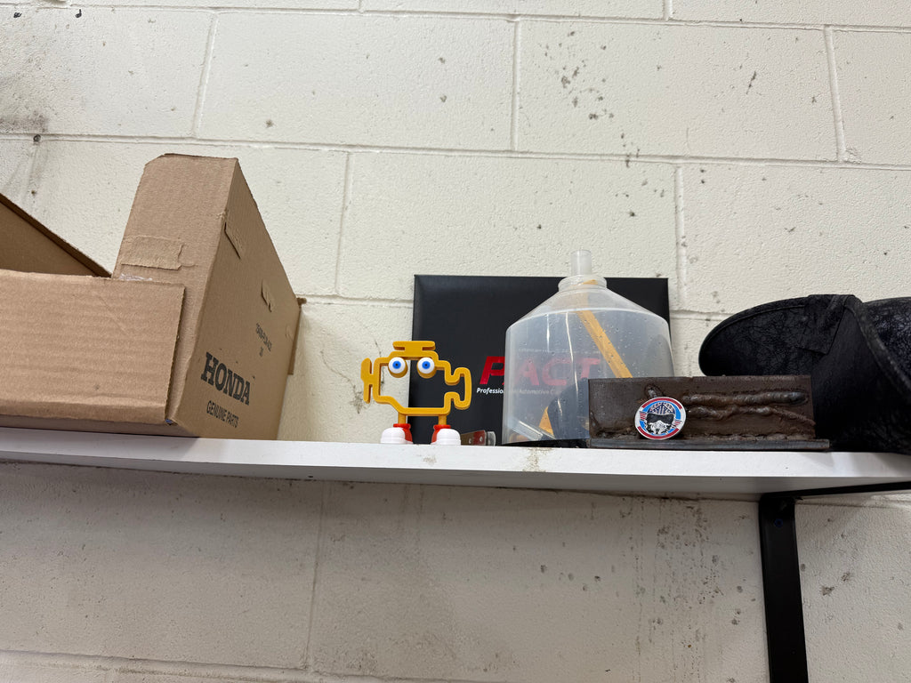 Shelf with various items including a Honda box, a small yellow figurine, and a clear container against a cinder block wall.
