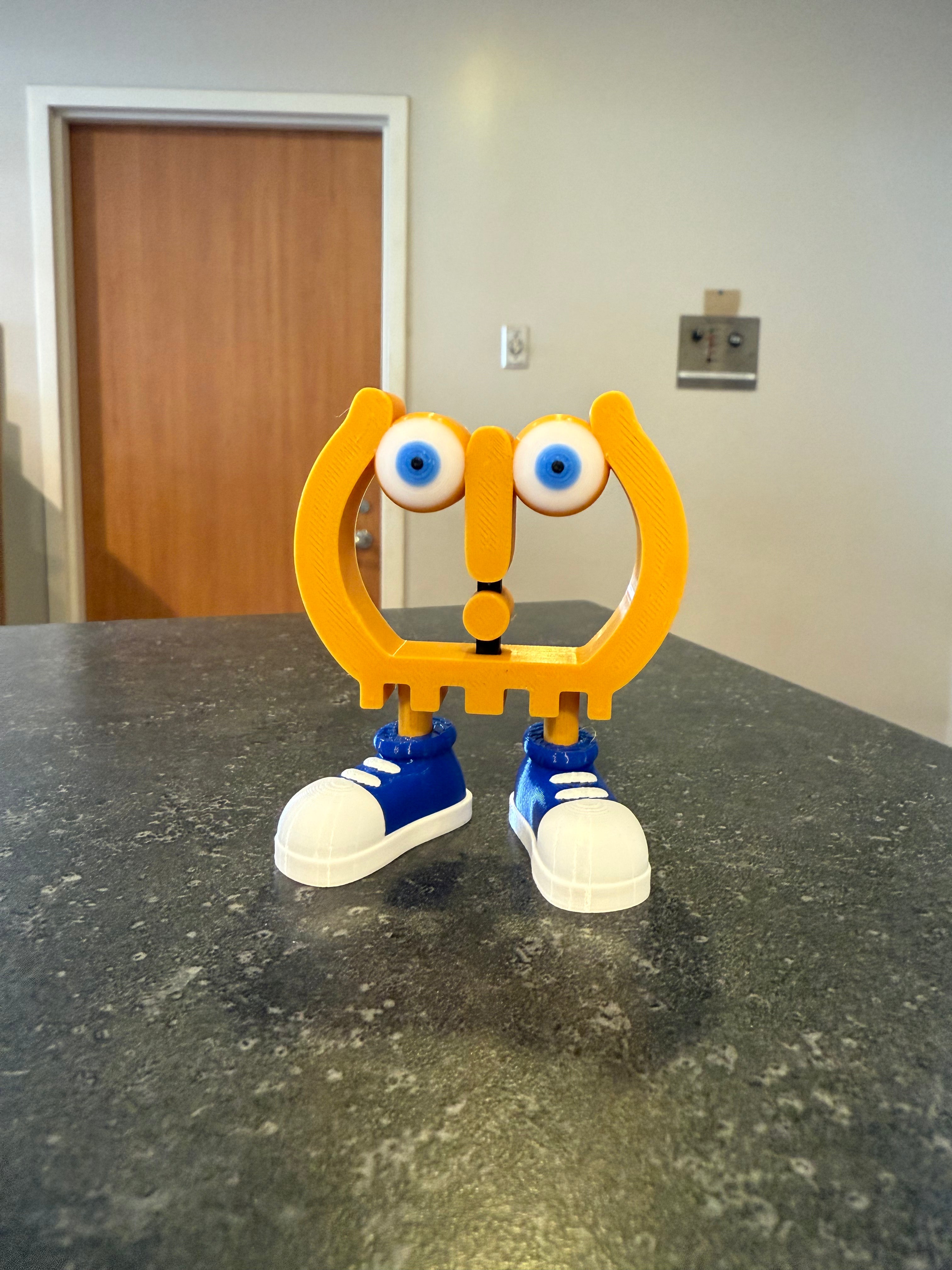 Toy figure with a yellow head, blue shoes, and white eyes on a dark surface.