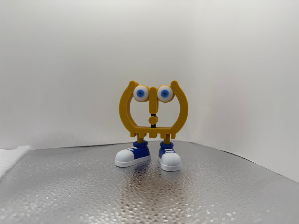 Toy figure with a yellow body, blue shoes, and large eyes on a reflective surface.