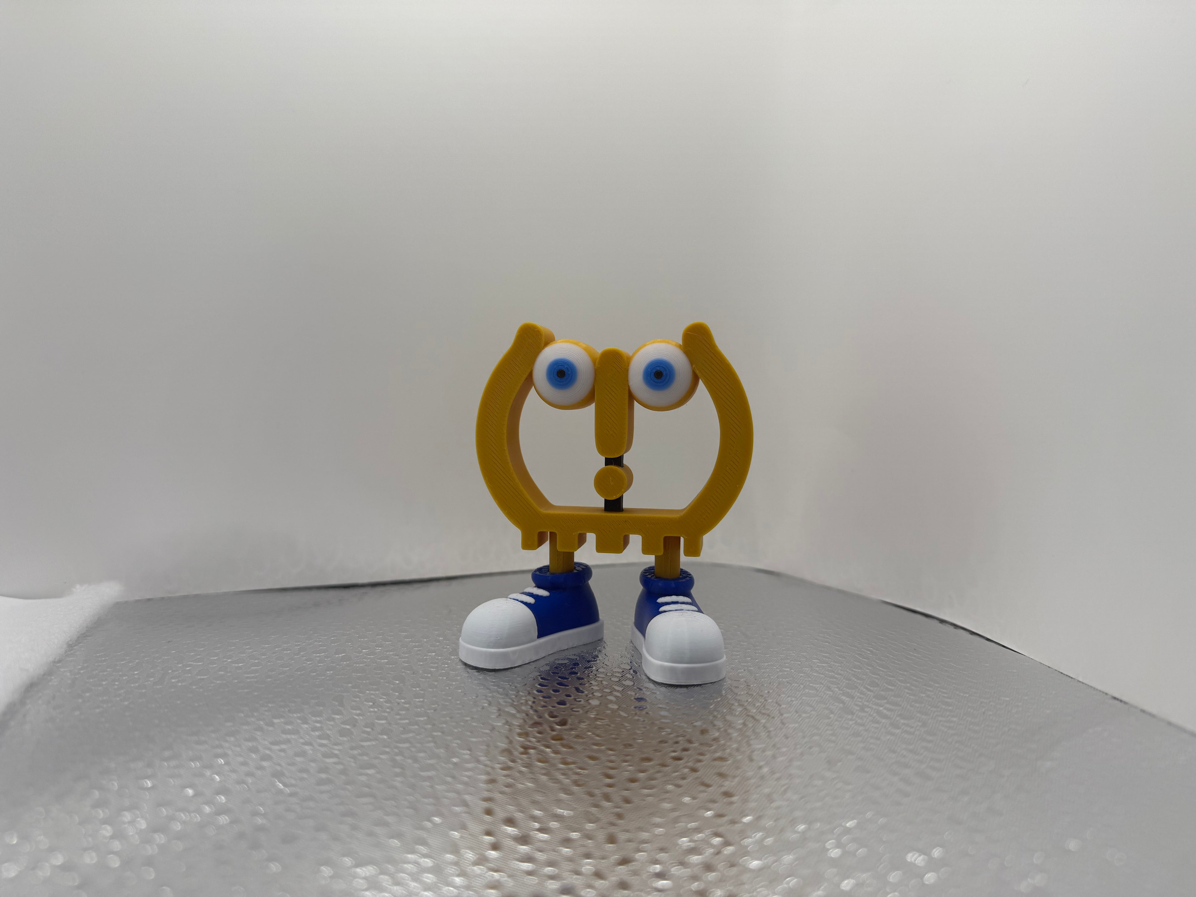 Toy figure with a yellow body, blue shoes, and large eyes on a reflective surface.