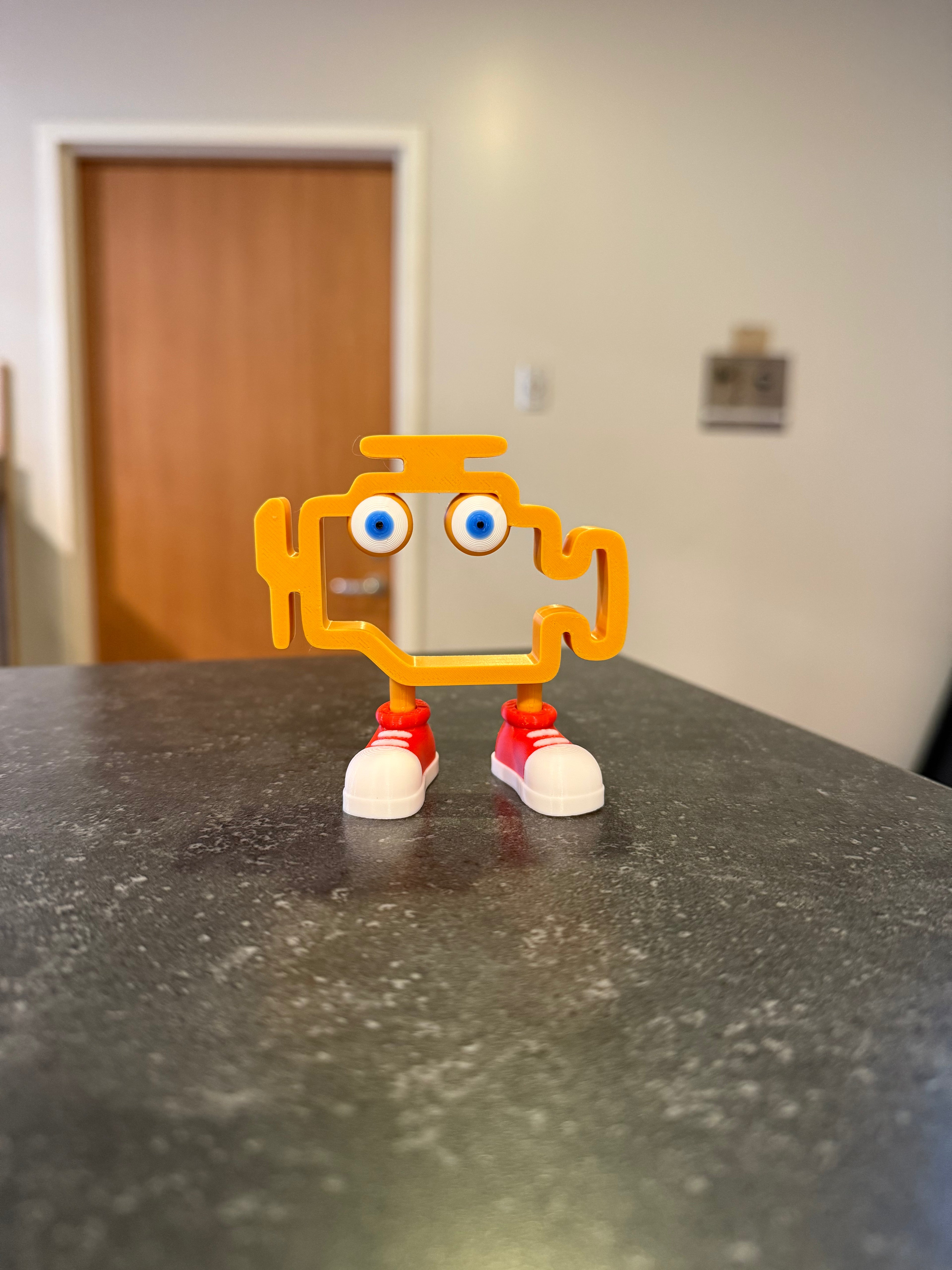 Toy engine with gold body, blue eyes, and red shoes on a dark surface